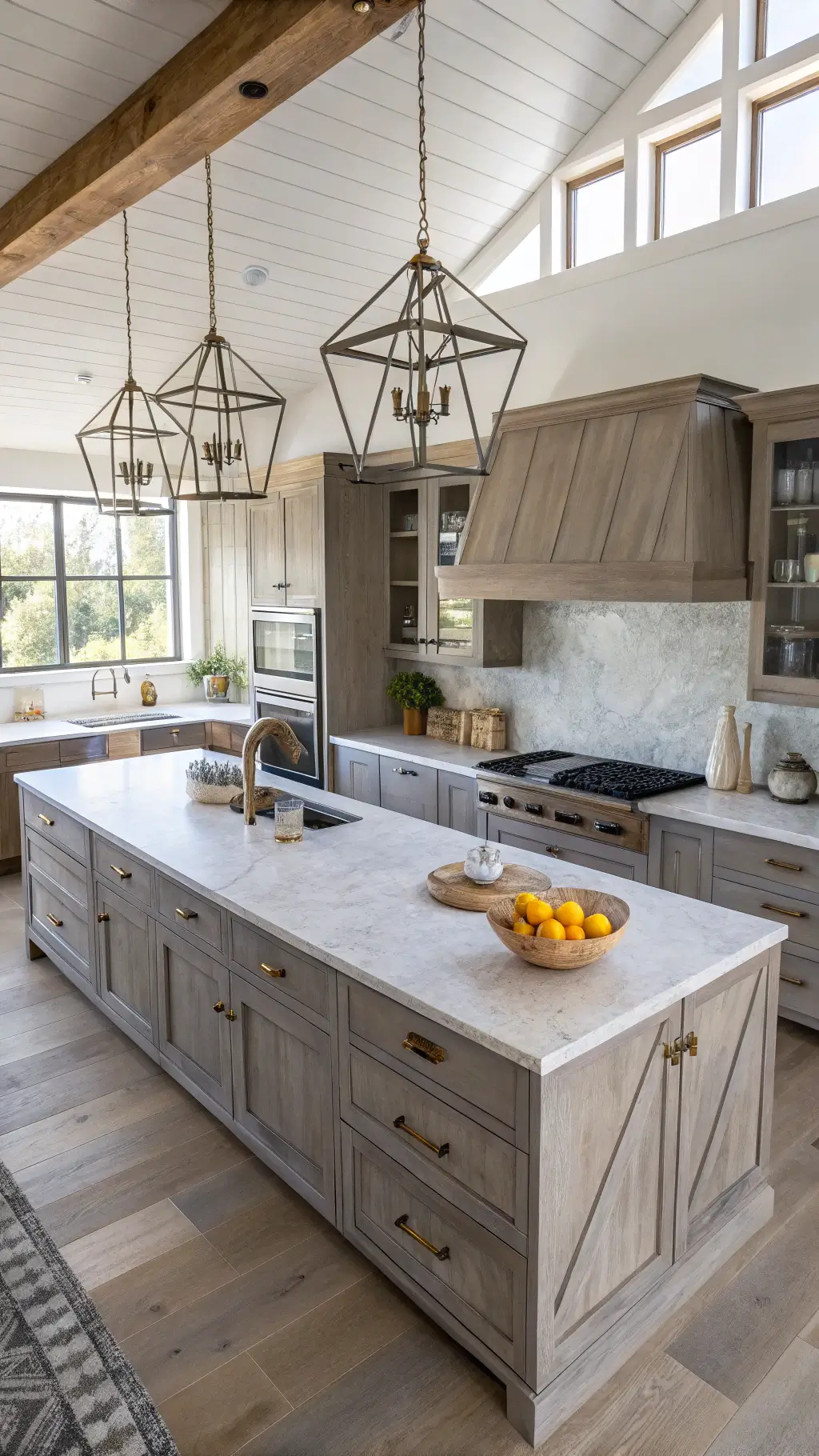 High-angle view of a modern-rustic kitchen with gray-washed oak cabinets, concrete countertops, and brass hardware, featuring a styled island and industrial glass pendants in soft midday light.