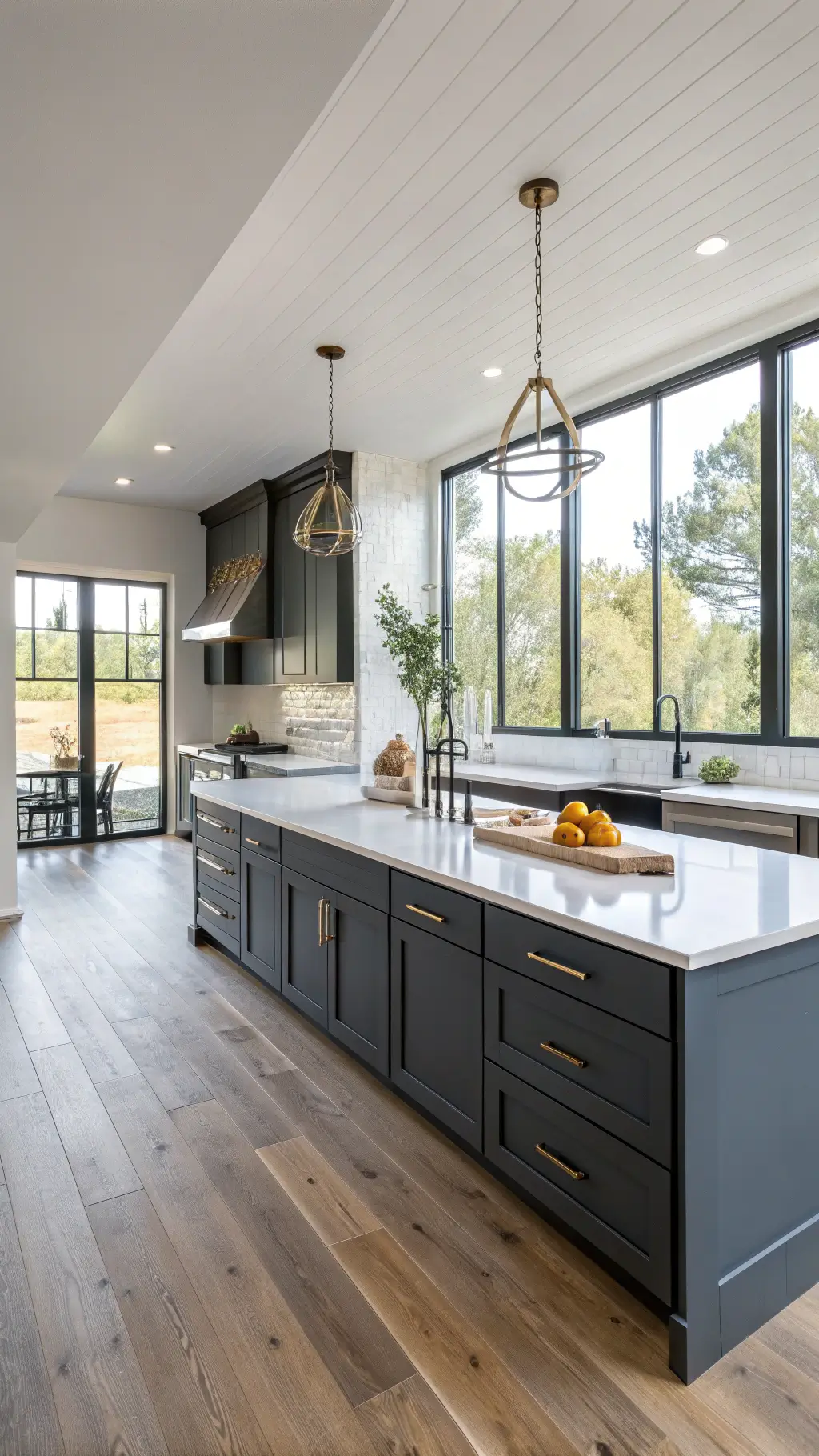 Contemporary 12x15ft kitchen with matte dark grey cabinets, white quartz countertops, brass hardware, honey oak floors, and morning light streaming through floor-to-ceiling windows.