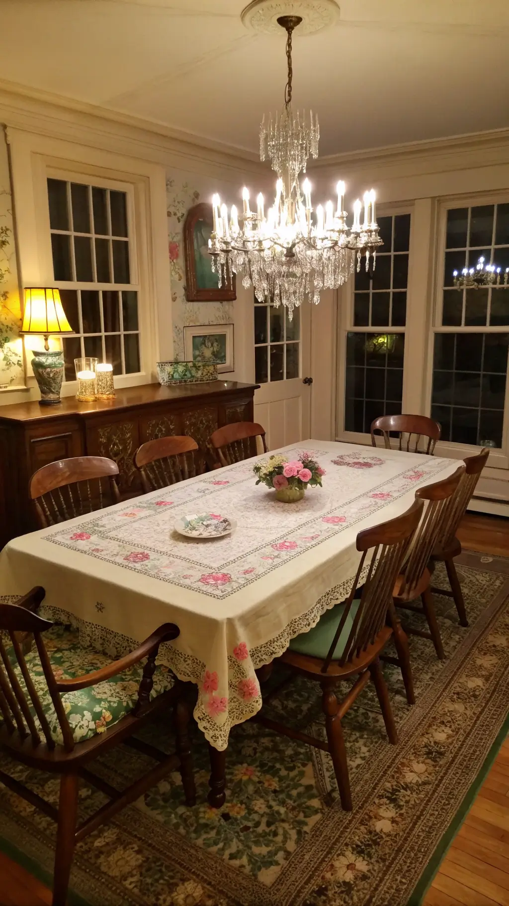 A cozy 14x16ft dining room at dusk featuring a heavy oak table with a hand-embroidered tablecloth and Depression glass collection, surrounded by Windsor chairs with needlepoint cushions, illuminated by a crystal chandelier casting prismatic light on wainscoted walls, creating a warm and intimate ambiance.
