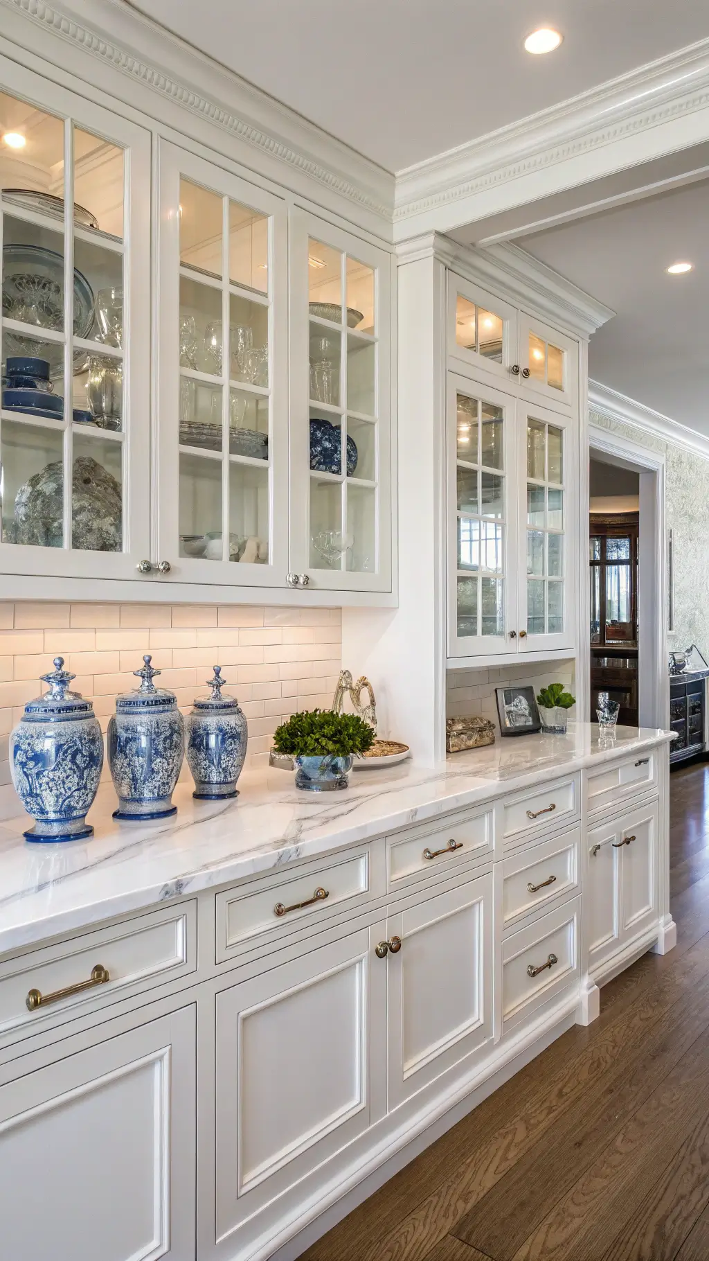 Elegant Hampton's kitchen with antique white cabinets, white oak island, marble subway tile, and polished nickel hardware, adorned with blue-and-white chinoiserie vases, crystal decanters and silver accessories, providing an atmosphere of refined coastal elegance.