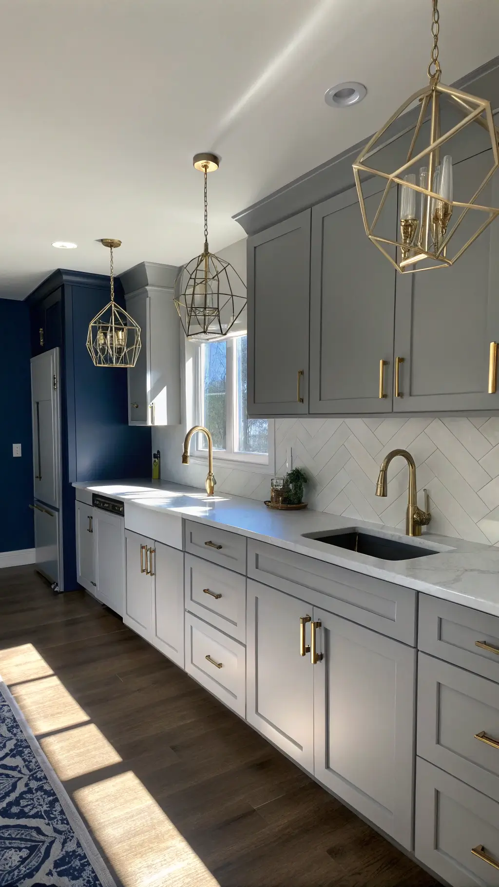 Modern kitchen with light gray cabinets, navy accent wall, brass fixtures, white countertops, and geometric pendant lights.