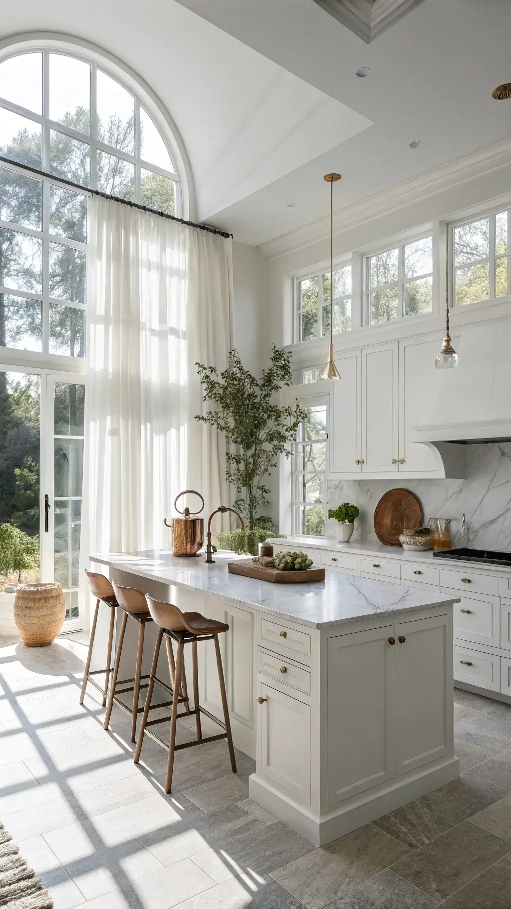 Contemporary white kitchen with sunlit marble countertops, Shaker cabinets, brass hardware, and a central island with acrylic stools, styled with herbs, ceramics, and a vintage copper kettle.