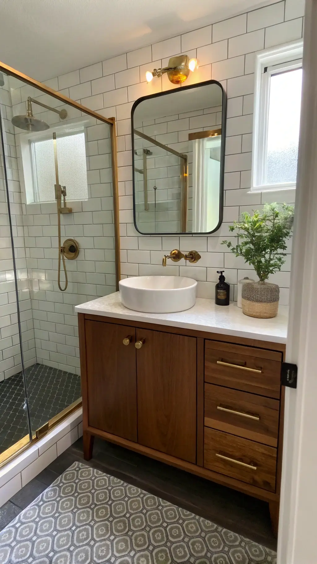 Compact bathroom with walnut vanity, brass fixtures, subway tile shower, and plant corner reflected in mirror at midday